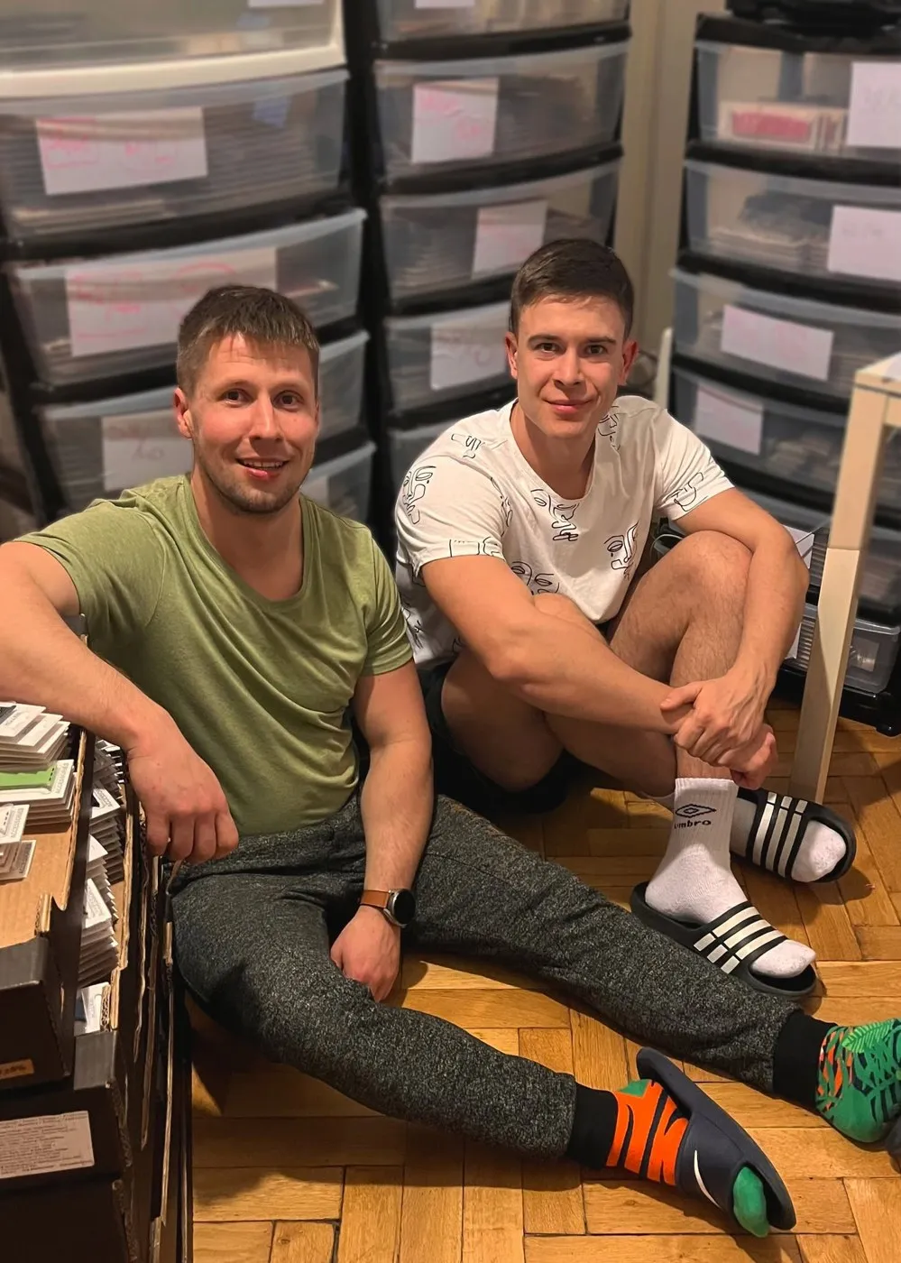 Filip a Tadeáš sedí na zemi bytu mezi regály plnými řemínků